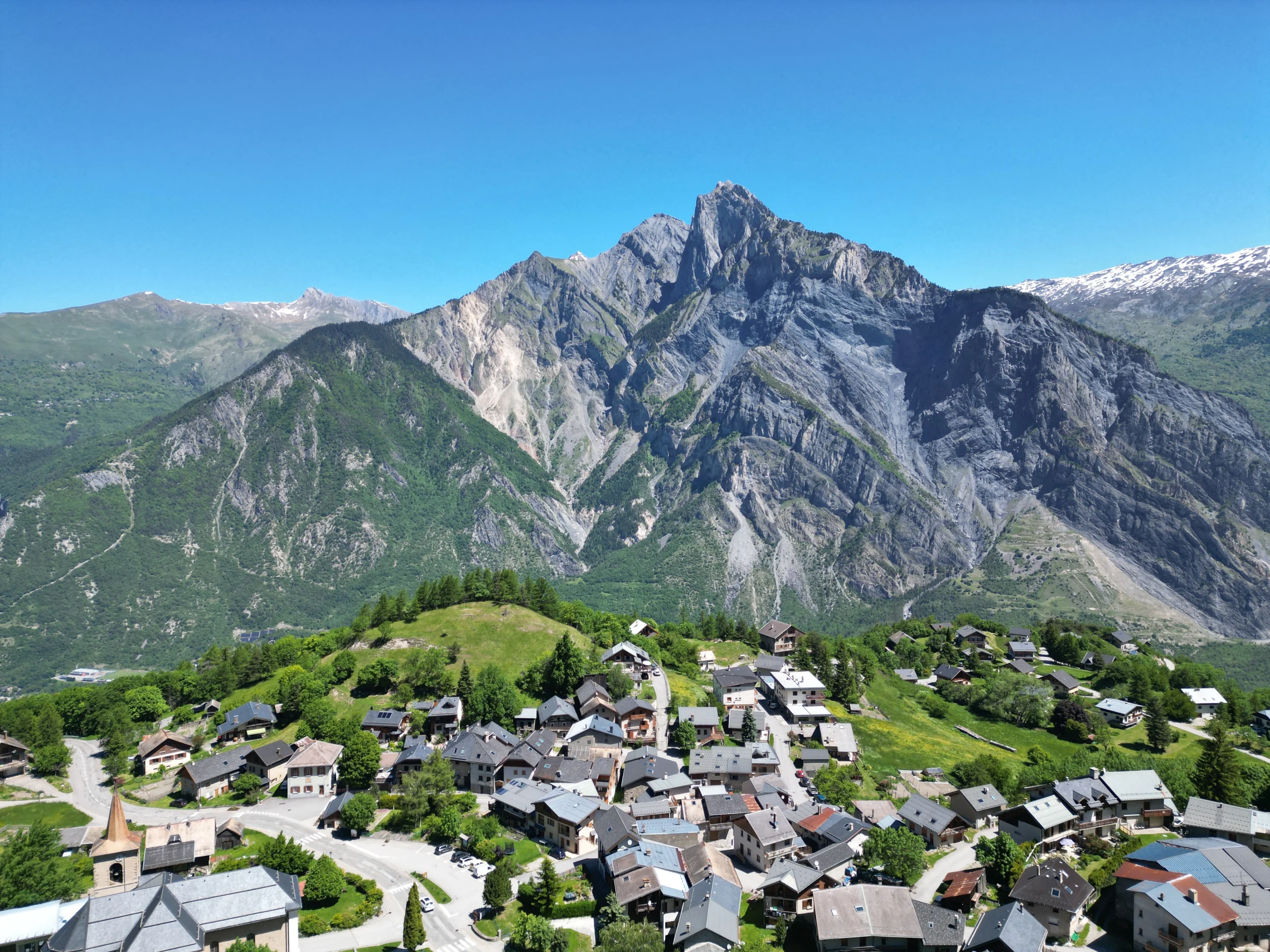 Vue d'ensemble de Montricher, hameau de montagne authentique situé en Maurienne, au-dessus de la station des Karellis, en Savoie. Perché à près de 1 600 mètres d’altitude, Montricher offre un cadre bucolique entouré de forêts de mélèzes et de pâturages. Ce lieu paisible est le point de départ idéal pour des randonnées familiales ou des balades nature vers le Gros Mélèze, la forêt communale ou les alpages. Son panorama dégagé sur les montagnes et sa tranquillité en font un lieu privilégié pour des vacances à la montagne, loin de l’agitation.