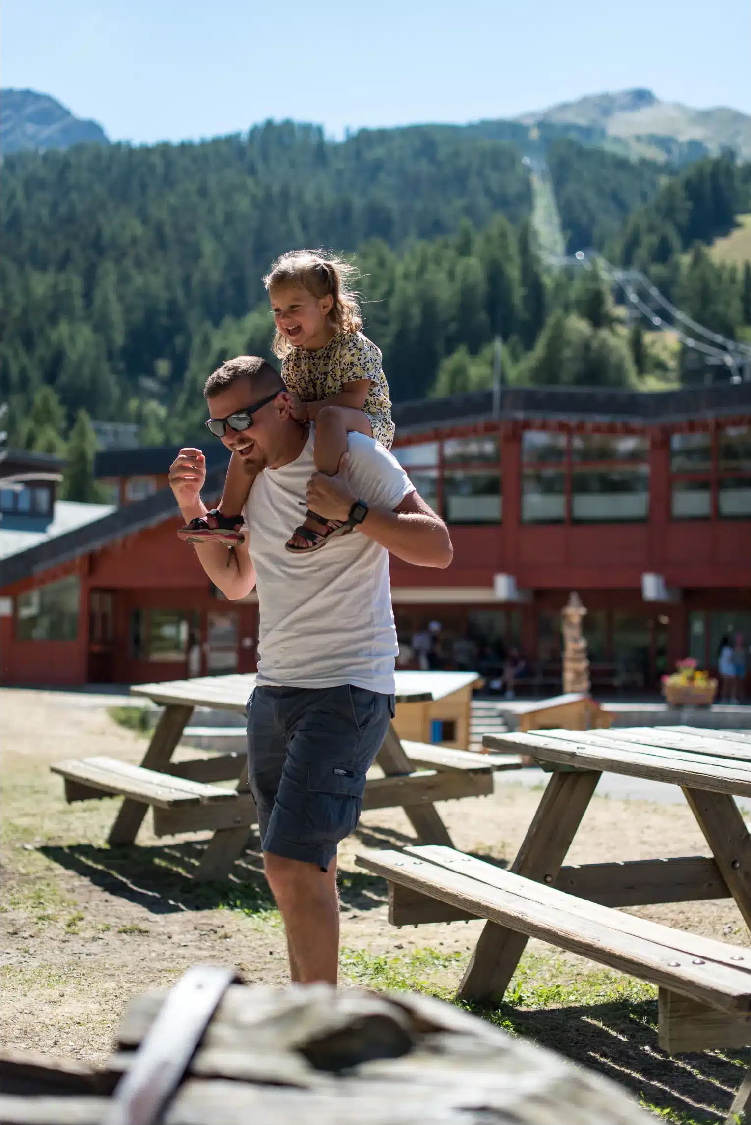 Père qui porte sa fille sur ses épaules autour de tables de pique nique